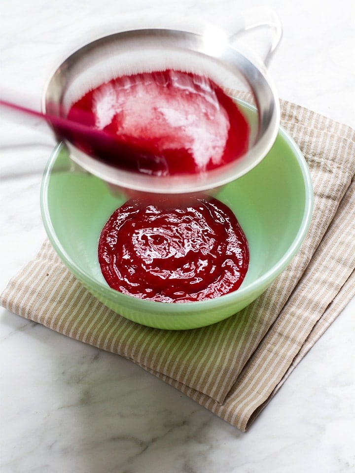 Passing raspberry puree through a sieve.