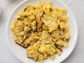 Horizontal closeup - a white plate with matzo brei eggs and matzo scrambled, on a white marble countertop.