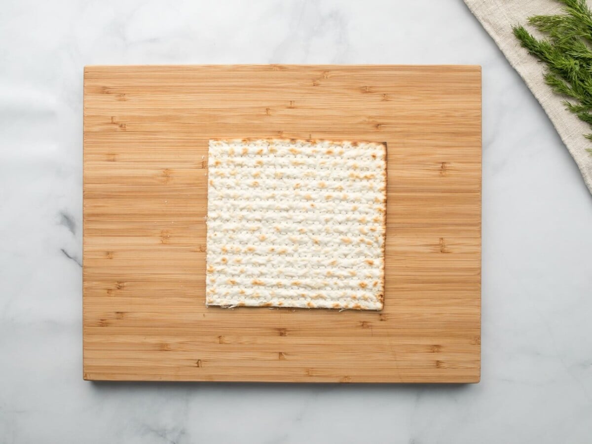 Horizontal overhead shot of a sheet of matzo laying on a wooden cutting board.