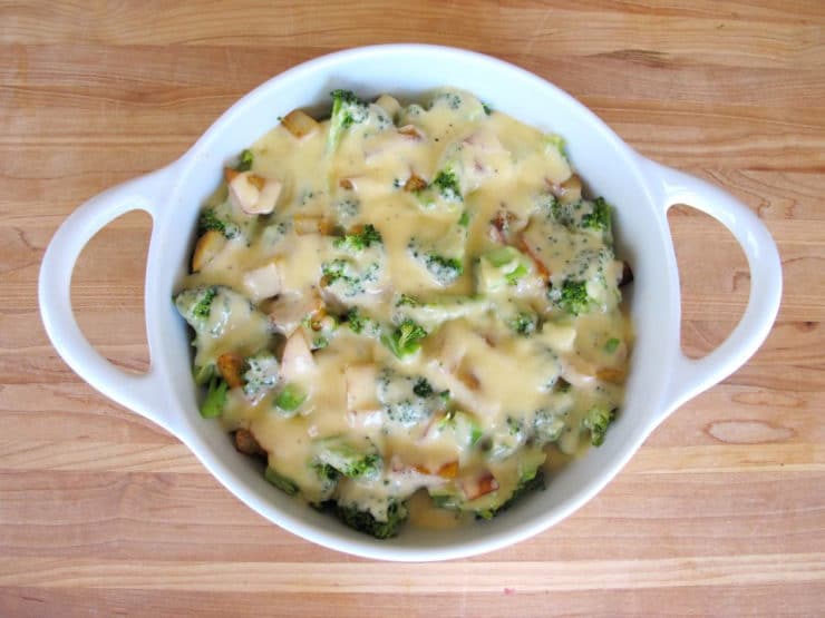 Broccoli Potato Gratin topped with melted cheese served on a huge white bowl with handles and on top of a table