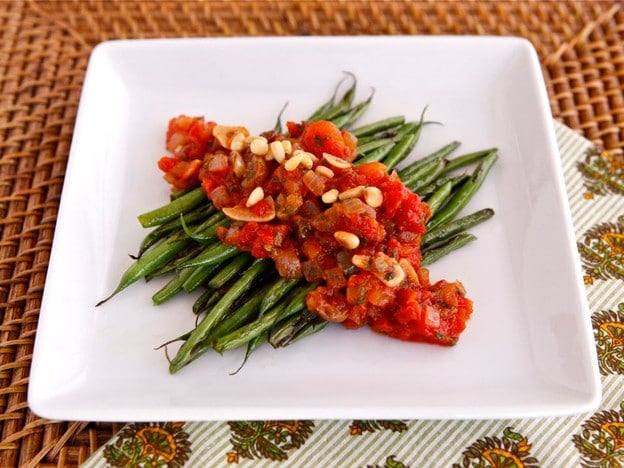 A plate of sauteed green beans topped with caponata sauce. 