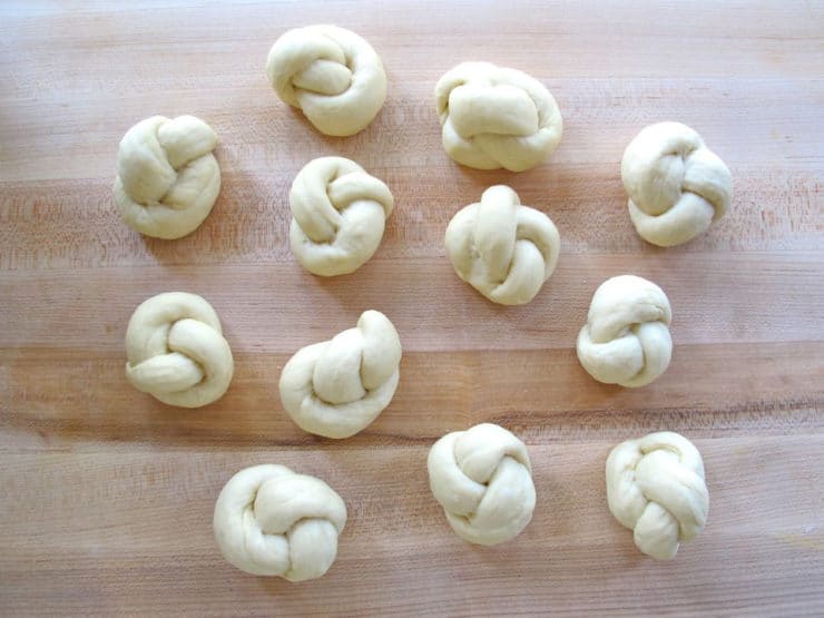 Knotted challah rolls on a board.