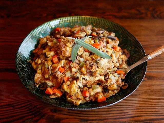 Thanksgiving Recipes by Tori Avey - Bowl of stuffing with sage garnish with spoon on wooden background.