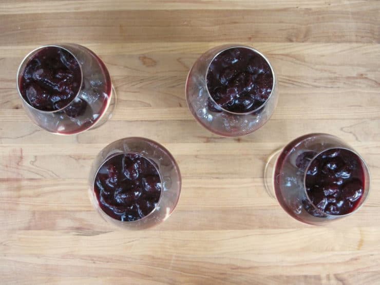 Adding cherry filling on top of cheesecake in glasses.
