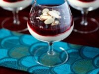 A Pinterest Pin of three glasses of cherry cheesecake shooters with almond slices on top, set on a vibrant blue cloth. Text reads, "Cherry Cheesecake Shooters."