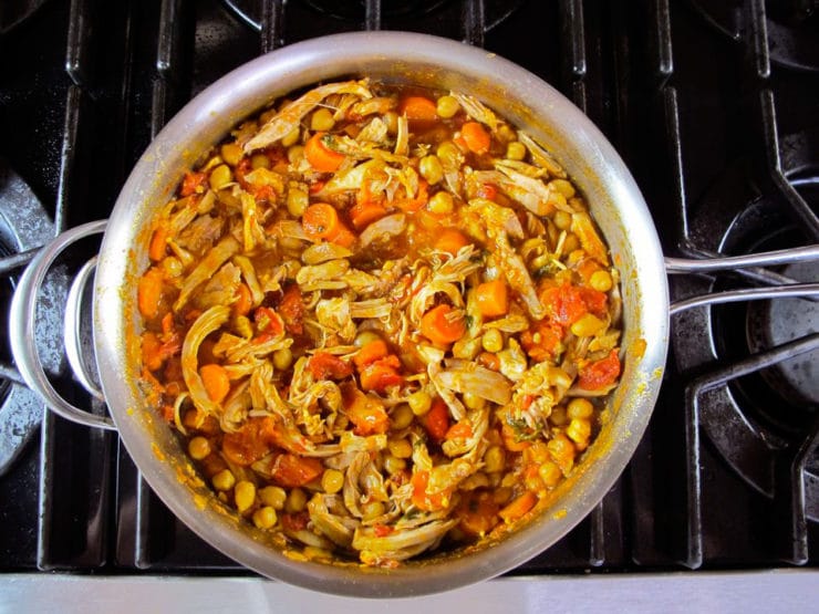 Shredded chicken added to stew in stockpot.