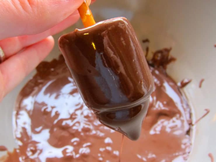 Hand dipping candy dreidel in melted chocolate.
