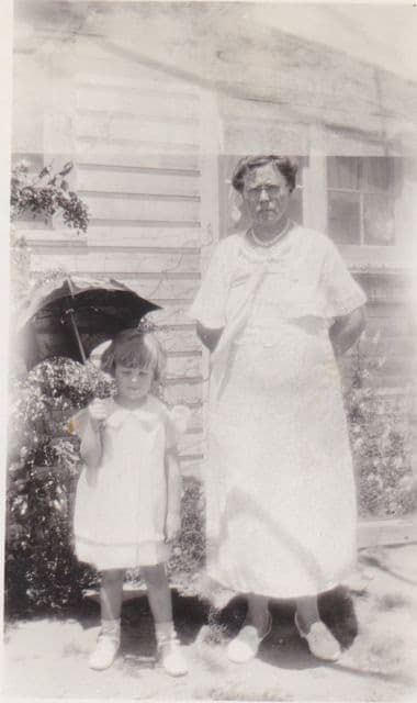 A black and white photo of a young girl holding an umbrella and a woman. 