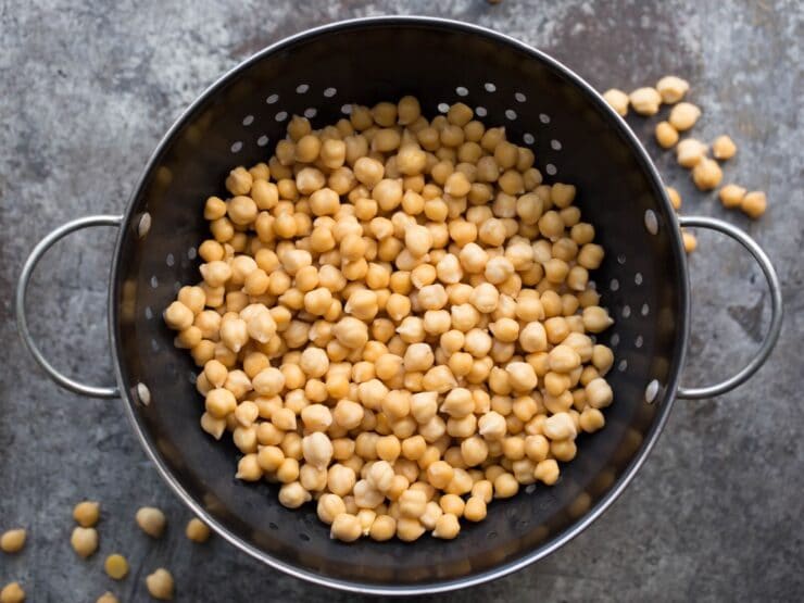 Cooked chickpeas in a colander on a grey background. 