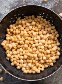 Cooked chickpeas in colander on a grey background.