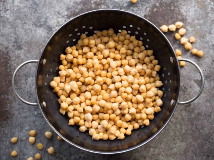 Cooked chickpeas in colander on a grey background.