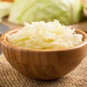 Bowl of fermented cabbage sauerkraut in wooden bowl with cabbage in background.
