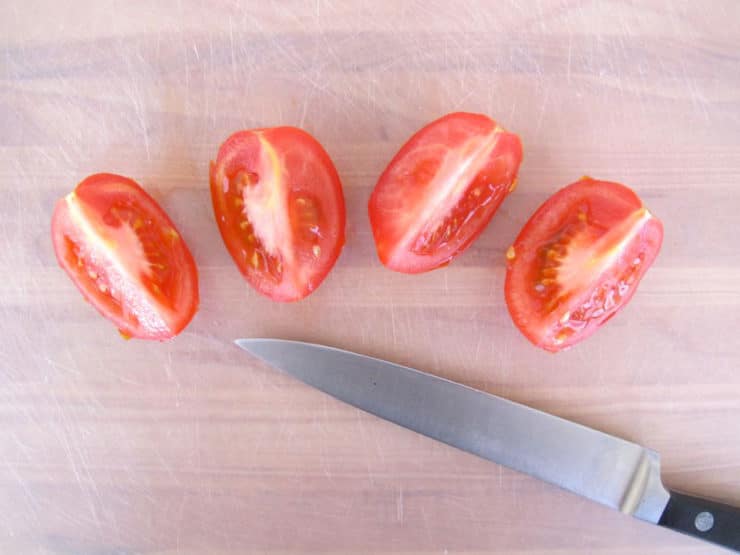 Four tomato quarters and chef's knife on cutting board.