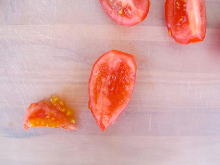 Tomato quarter without seeds, seed pulp beside it on cutting board.