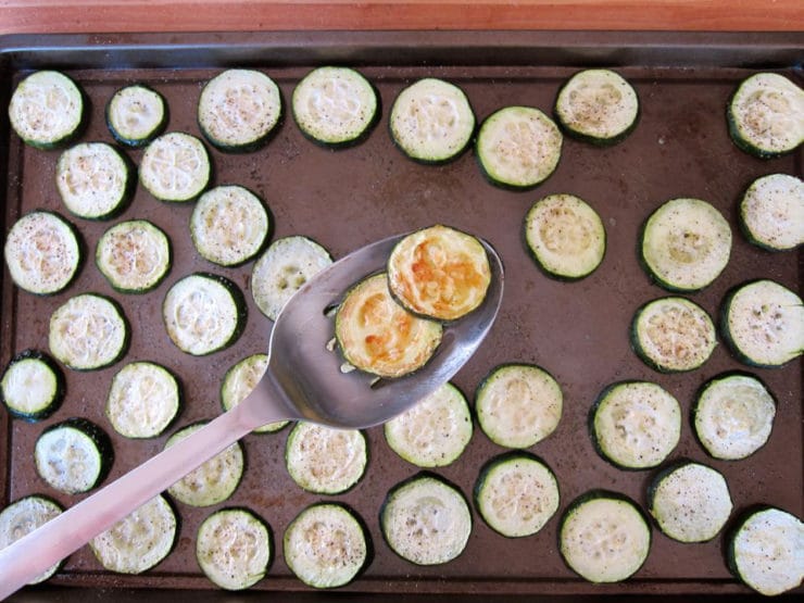 Flipping over sliced zucchini on a baking tray.