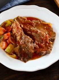 Overhead view of A slice of beef brisket next to a side of vegetables and topped with gravy on a round white plate.