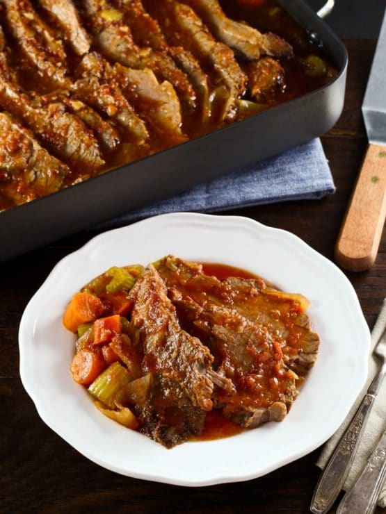 Overhead shot of A slice of beef brisket next to a side of vegetables and topped with gravy on a round white plate.