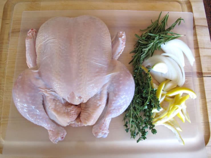 Whole chicken and aromatics on a cutting board.
