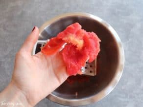 Skin of tomato held in hand over bowl after grating.