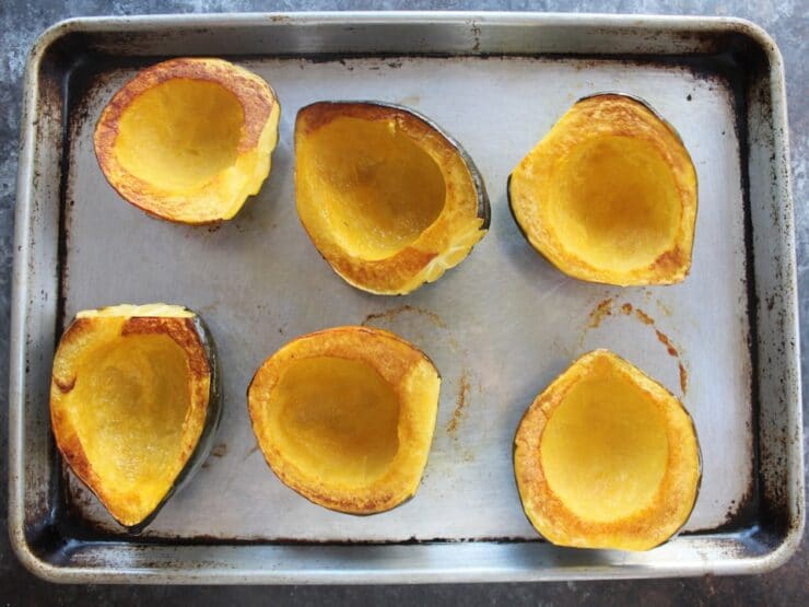 Baking sheet of roasted acorn squash halves with golden brown edges, flesh side facing upward.