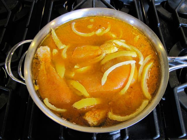 Chicken quarters simmering in stock in a saucepan.