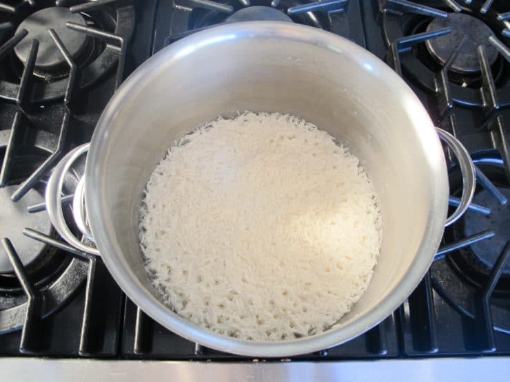 A pot of cooked white rice sits on a stove with black grates.
