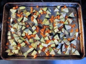 Chopped eggplant and carrots are spread evenly on a baking sheet, ready to be roasted in an oven.