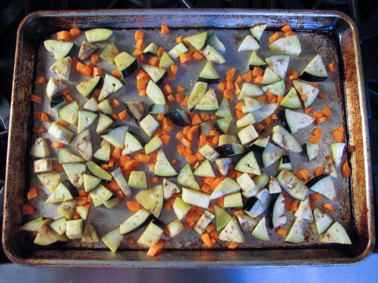 Chopped eggplant and carrots are spread evenly on a baking sheet, ready to be roasted in an oven.