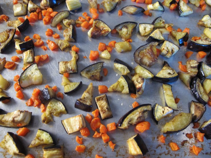 Close up view of chopped and cooked eggplant and carrots that are spread evenly on a baking sheet.