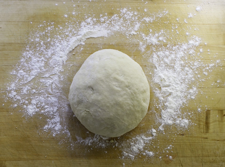 A ball of smooth dough rests on a floured wooden surface.