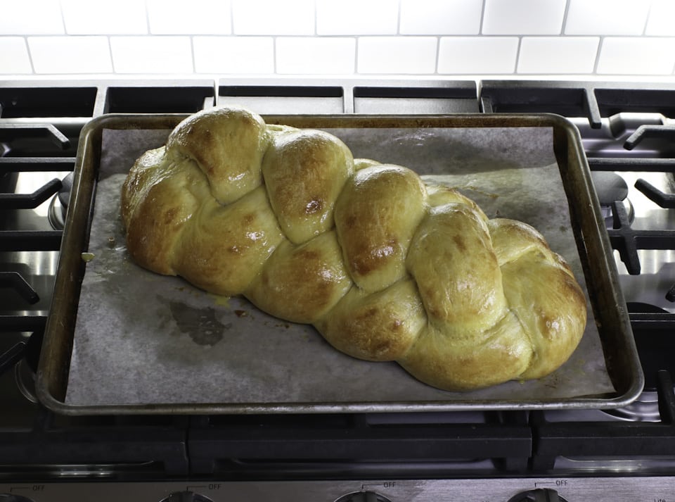 A golden-brown braided challah bread placed on a baking sheet, emphasizing its beautiful shape and crusty exterior.