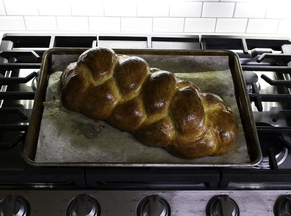 A dark golden-brown braided challah bread placed on a baking sheet, emphasizing its beautiful shape and crusty exterior.