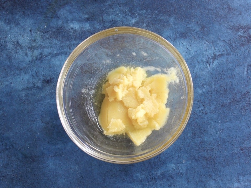 Solid schmaltz chicken fat collected from chilled stock in small glass bowl on blue countertop.