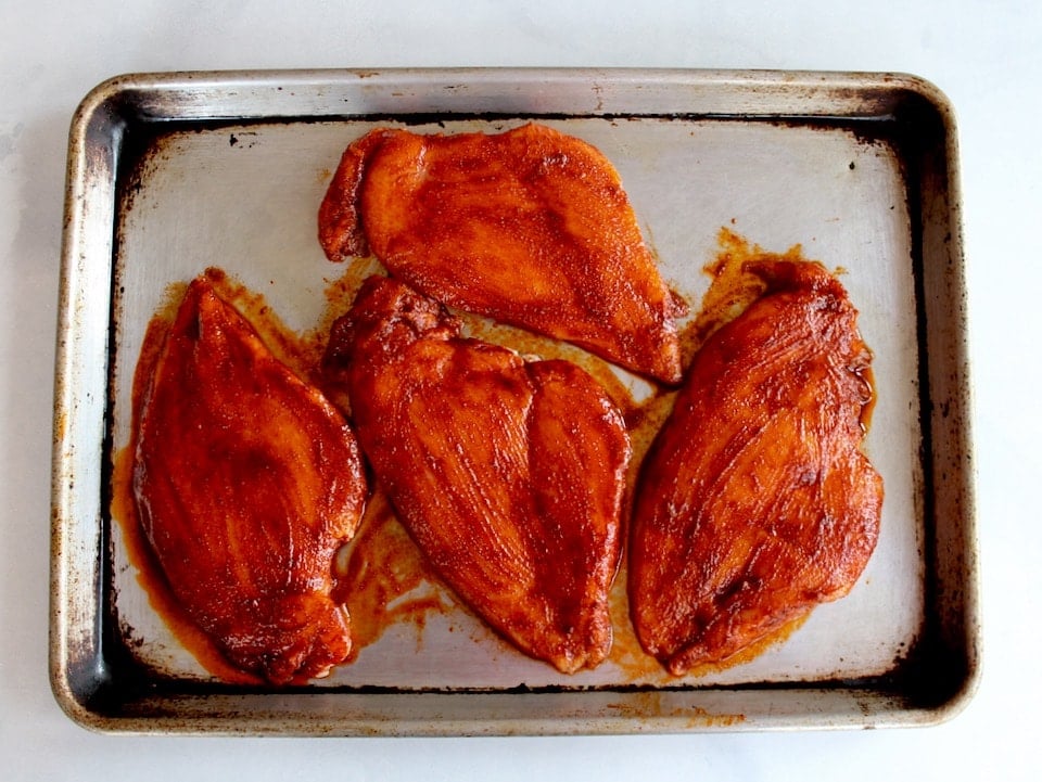 4 flat pounded chicken breasts brushed with paprika marinade on a baking sheet.