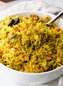Vegetable rice in white bowl with spoon on white cloth background.
