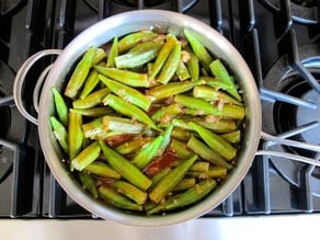 Pouring tomato sauce over cooked okra.