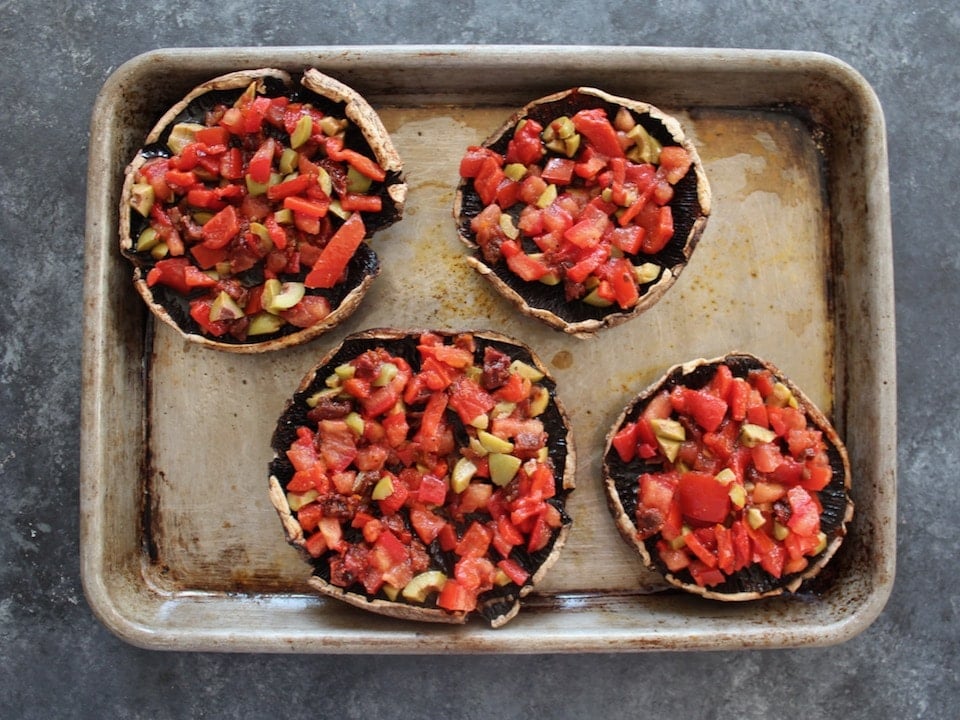 Vegetable-stuffed portobello caps, four on a baking sheet.