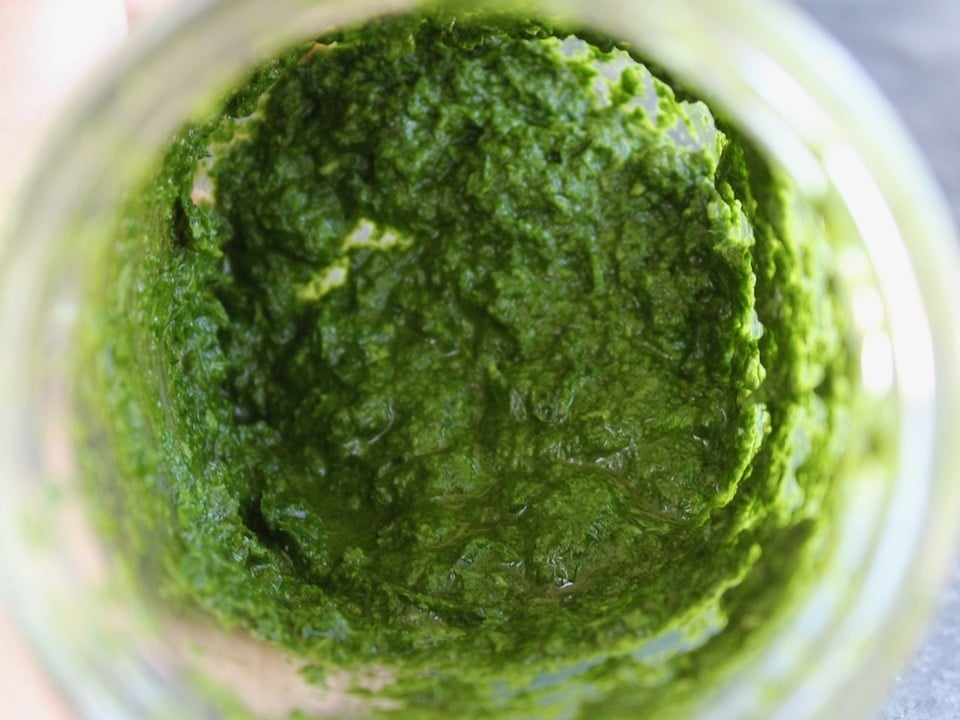 Close up shot of fresh basil pesto inside of a glass mason jar.