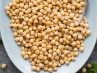 How to Soak and Cook Chickpeas Pinterest Pin - a large oval dish of cooked chickpeas garnished with fresh parsley, with a serving spoon.
