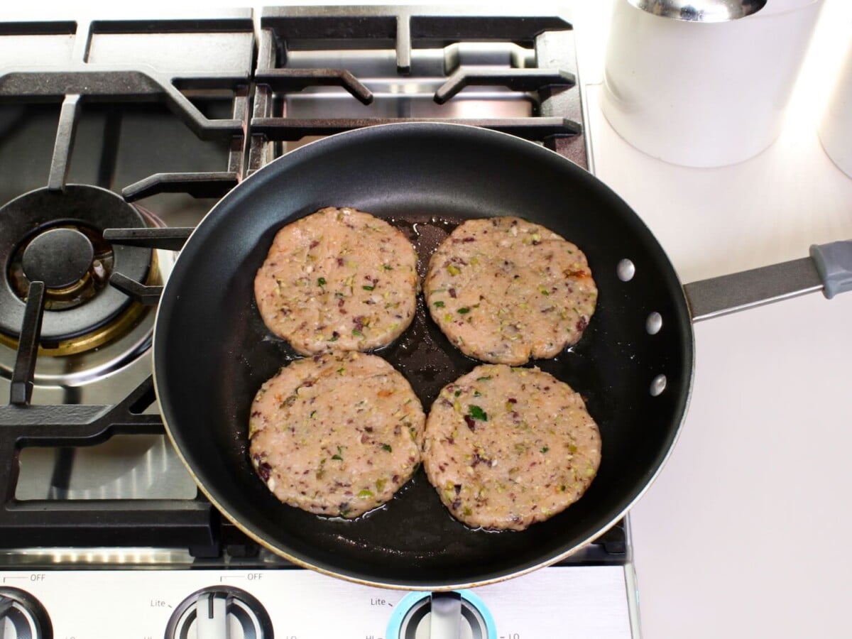 Overhead shot of four turkey burger patties in a frying pan.
