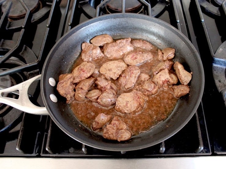 Browning chicken livers in liquid schmaltz in skillet on stovetop.