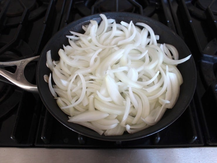 Large skillet full of uncooked sliced onions on stovetop.