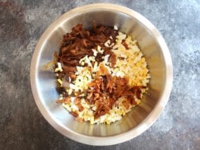 Stainless steel bowl filled with cooked chicken livers, diced hard boiled eggs, gribenes, caramelized onions.