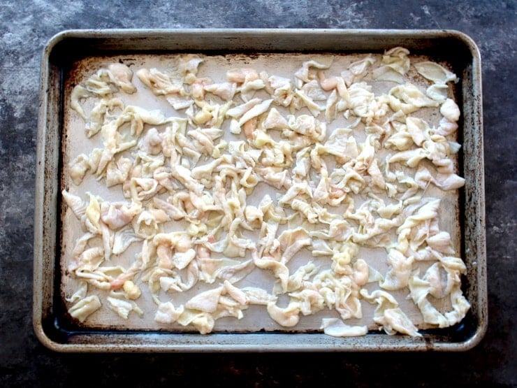 Raw chicken skin pieces on a baking sheet tray.