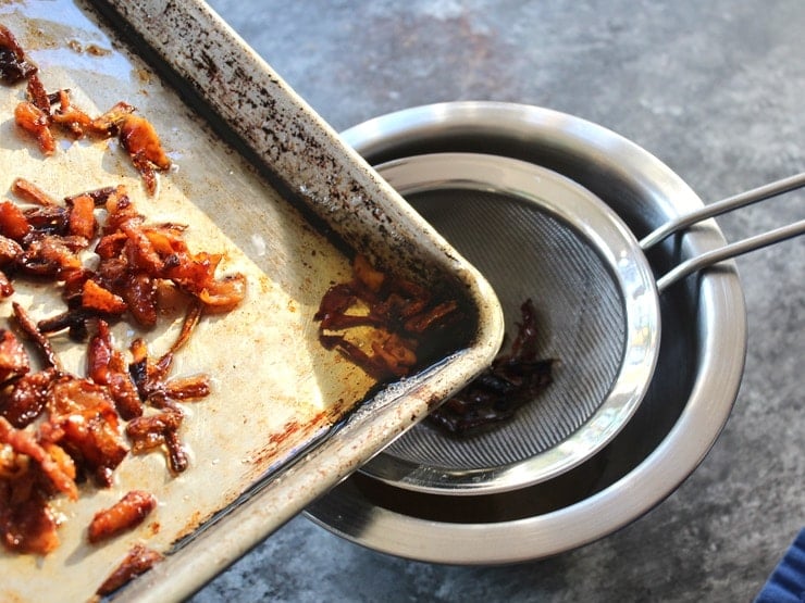 Baking sheet with schmaltz and gribenes, pouring rendered chicken fat into mesh strainer.