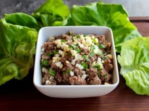 Front angle shot - dish of chopped liver garnished with chopped hard boiled egg and fresh parsley, with lettuce on a wooden cutting board.