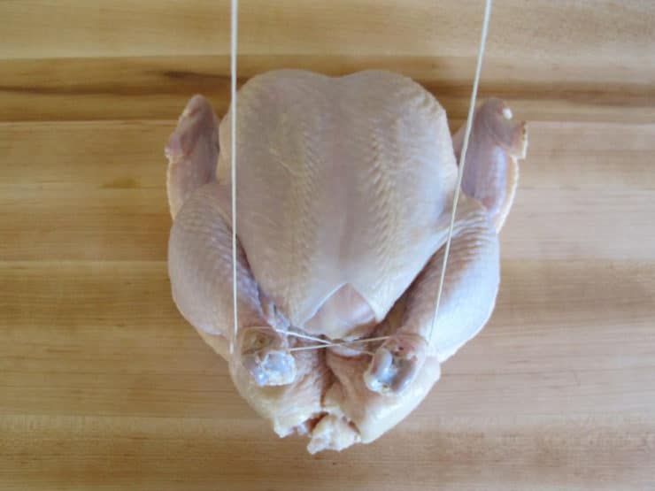 Whole chicken on cutting board - trussing strings looped around drumsticks.