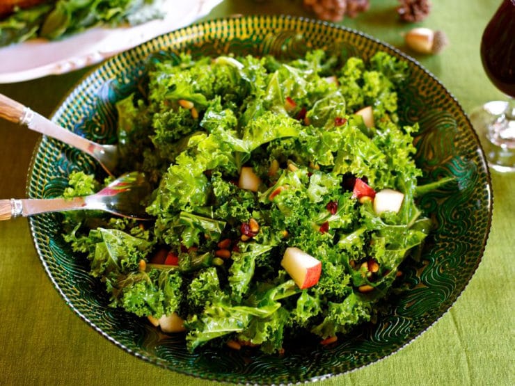 Kale, Pear and Cranberry Salad in a bowl with serving spoons sticking out. 