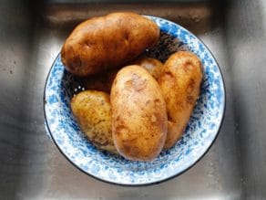 Five large Russet potatoes in blue speckled colander over sink.