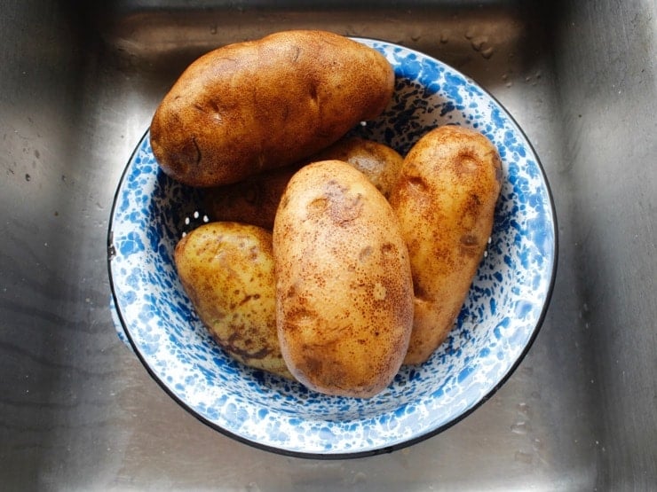 Five large Russet potatoes in blue speckled colander over sink.